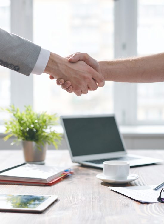 Handshake of two young business partners over desk with office supplies after signing contract at meeting
